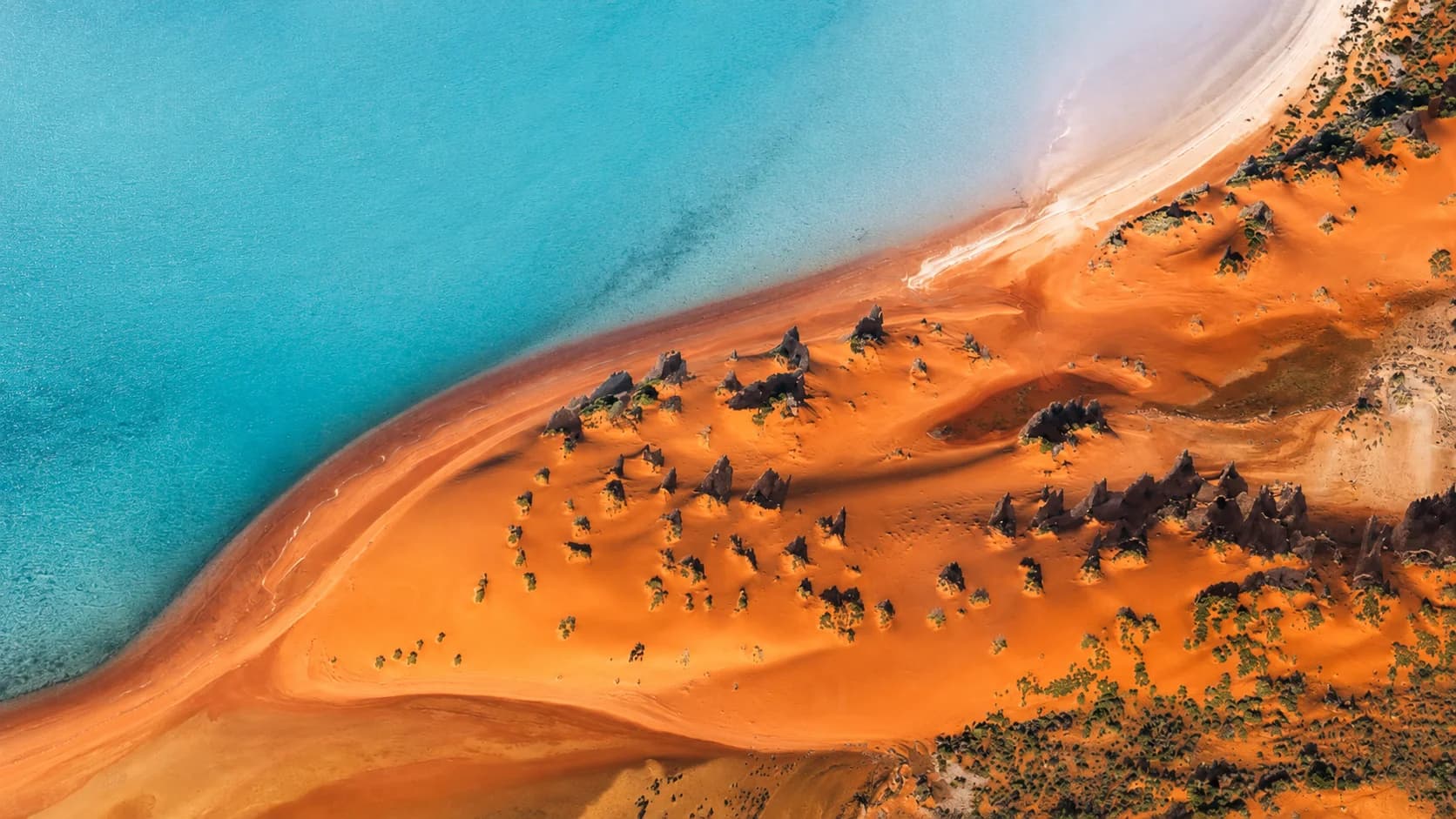 Aerial view of a turquoise coastline meeting an ochre sand peninsula